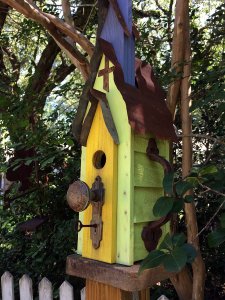 A lime green bird house with a tin roof and yellow door