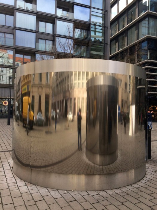Buildings, people and cars reflected in a metallic surface