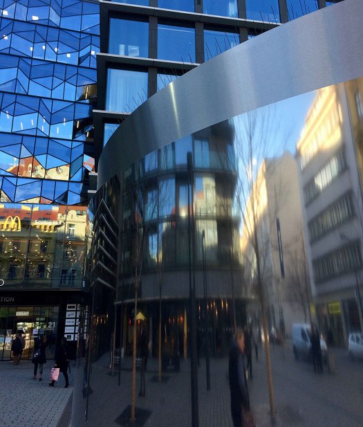 Buildings, people and cars reflected in a metallic surface