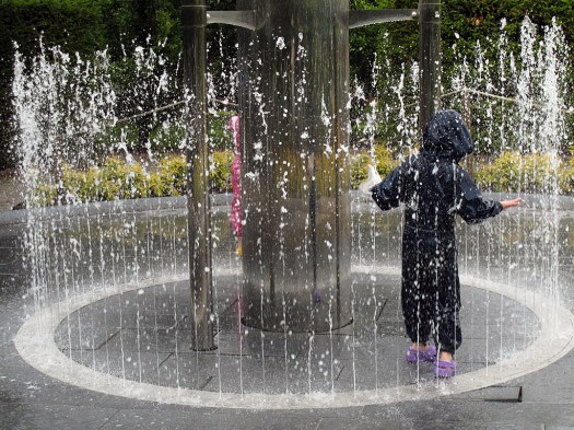 A child in waterproofs plays in a circle of water jets