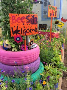 Signs in a flower bed with pink, purple and turquoise tyre planter