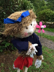 Scarecrow with pink cheeks, a blue ribbon and a flower