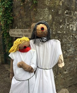 Male and female chorister scarecrows beside a church signpost