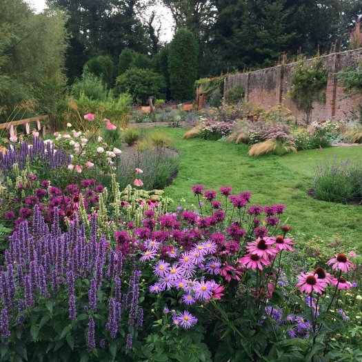 A fenced flower garden along a long, tall brick wall