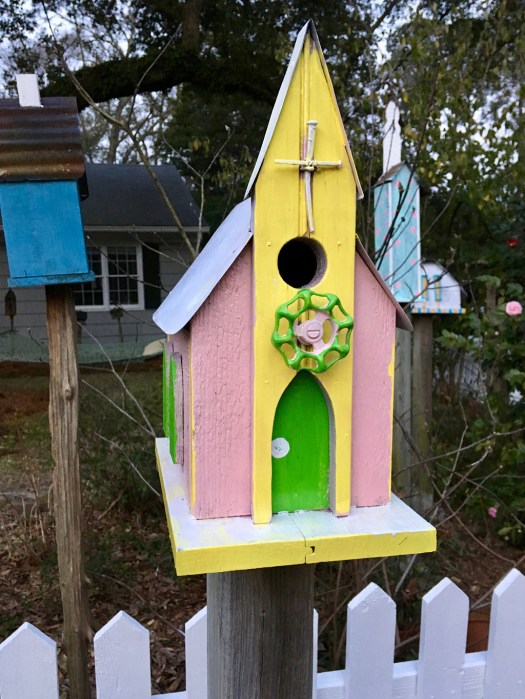 Pink, yellow and lime green birdhouse with a church steeple