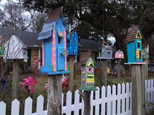 Brightly coloured birdhouses on wooden poles with a white picket fence