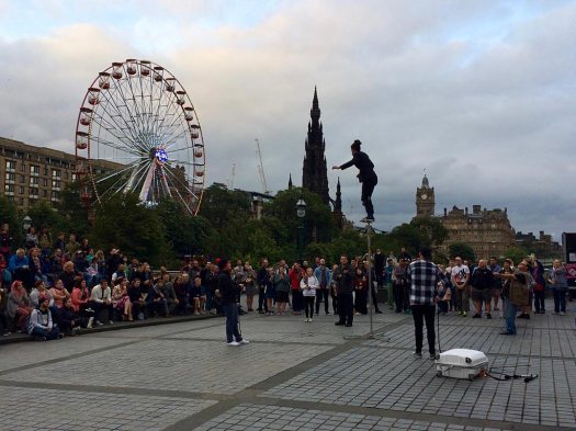 Street entertainer balances on a pole watched by an audience