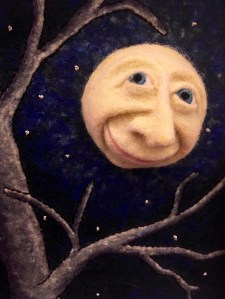 A felt man in the moon shines through the branches of a tree