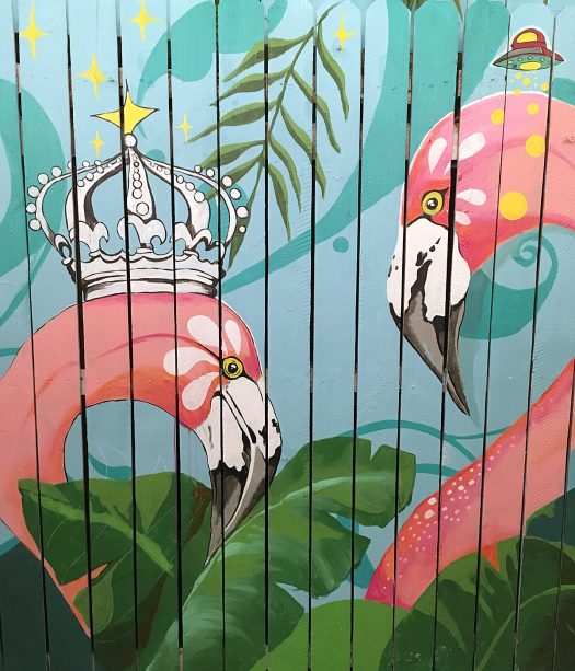 Pink flamingos, one with a crown, painted on a fence