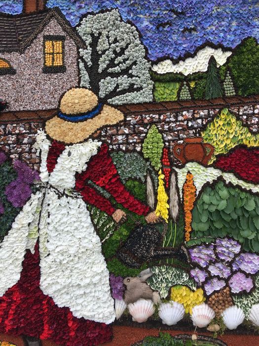 Well dressing: girl in a pinafore watering flowers in a walled garden