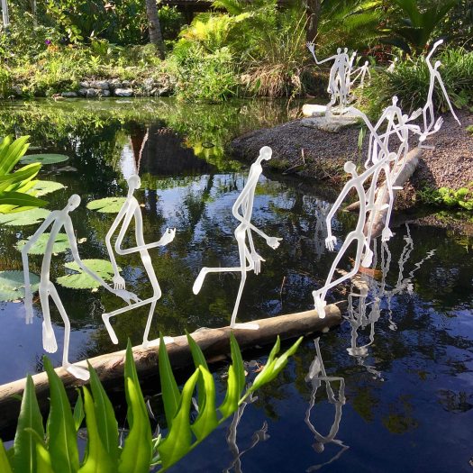 Elongated glass men crossing water by Hans Godo Fräbel