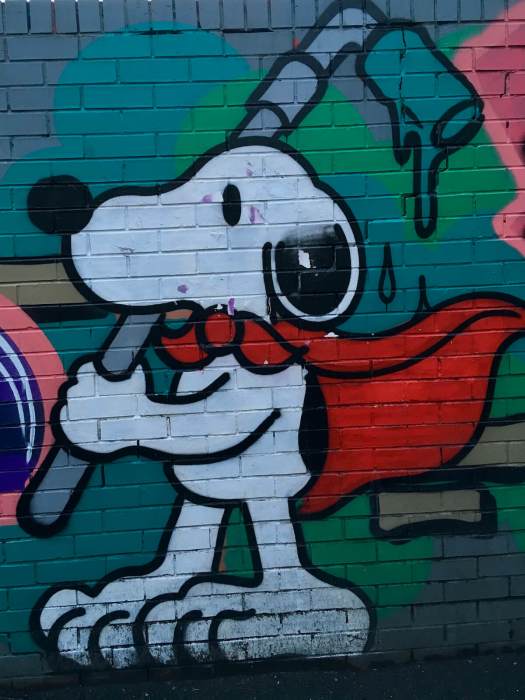 Graffiti of Snoopy with red cape and paint roller on a brick wall