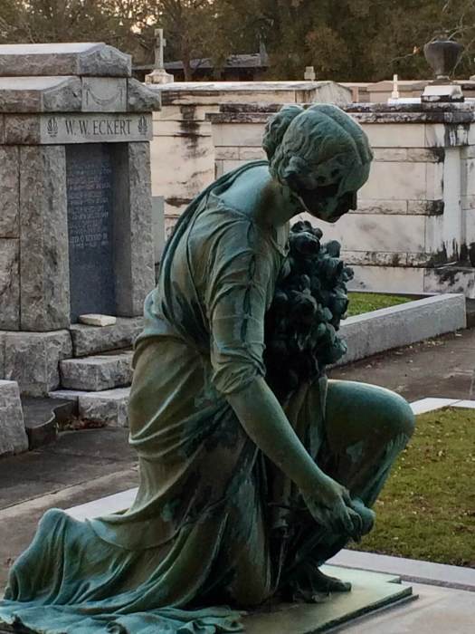 Statue of a lady laying roses on a grave