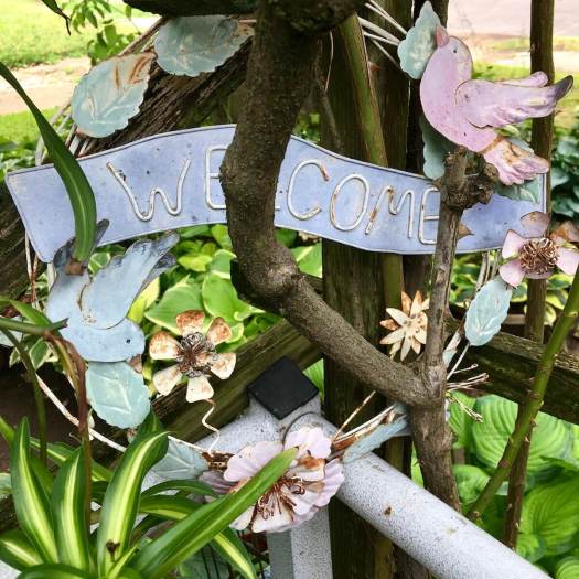 Metal welcome sign with birds and flowers in a garden