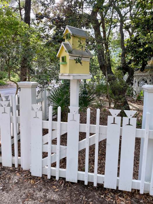Picket fence with yellow birdhouse on a tall post