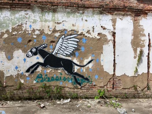 Winged mule on a crumbling wall with stars, painted over the word Blessissippi