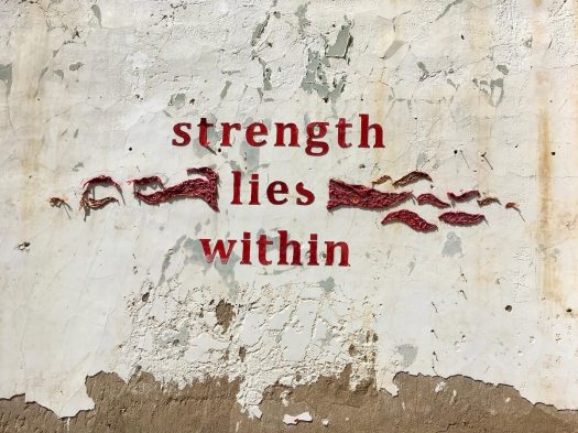 Strength Lies Within artwork on a flaking plaster wall by Church Goin Mule