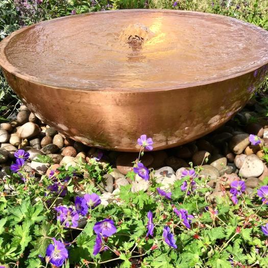 Copper bowl overspilling water on to pebbles