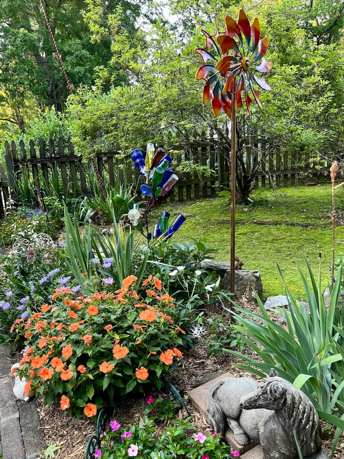 Tall wind spinner, a bottle tree and a concrete horse in a garden