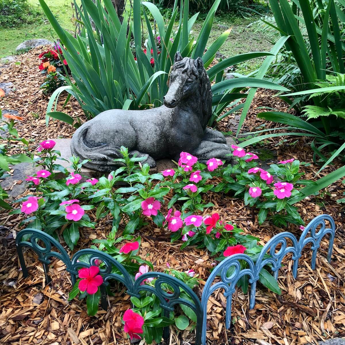 Horse lying on a low plinth with irises and vincas and decorative edging
