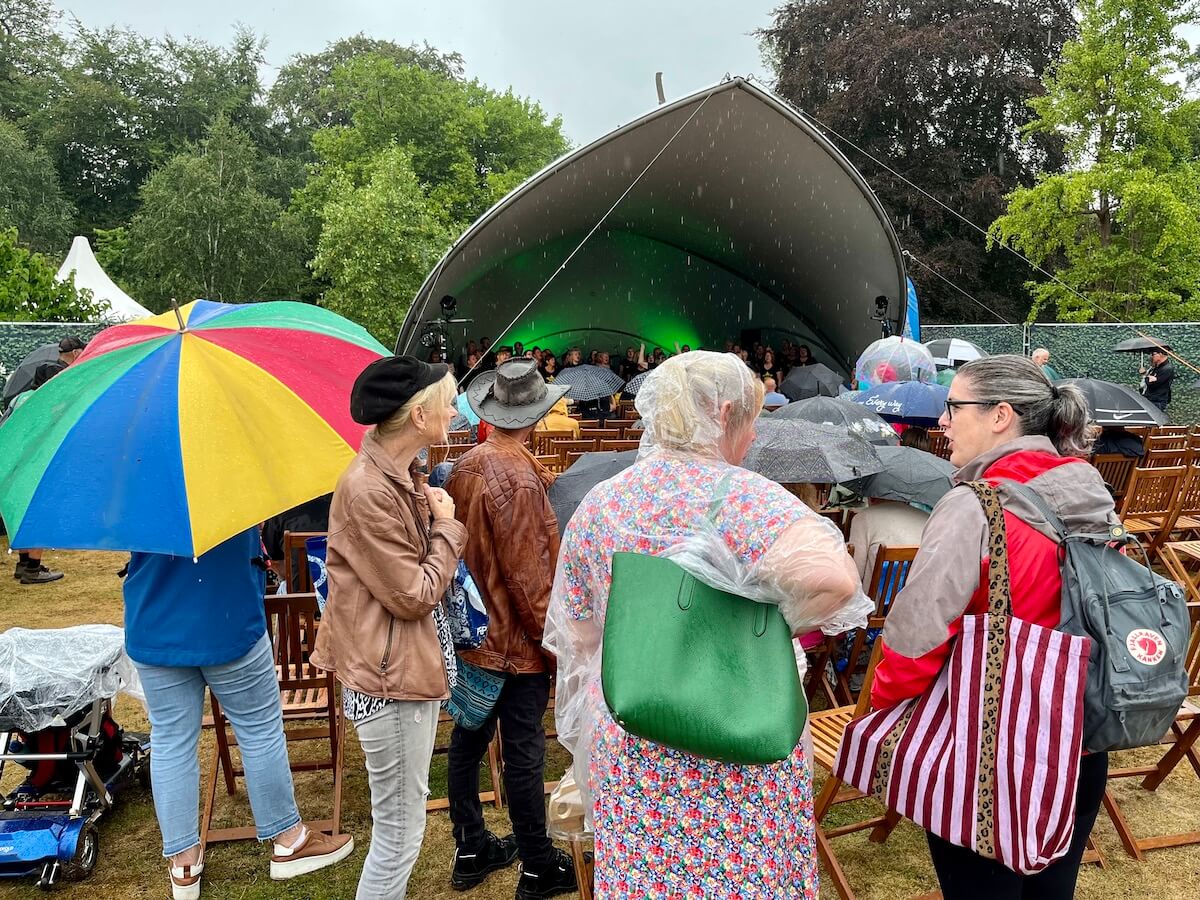 Singers under an awning, with listeners in the rain