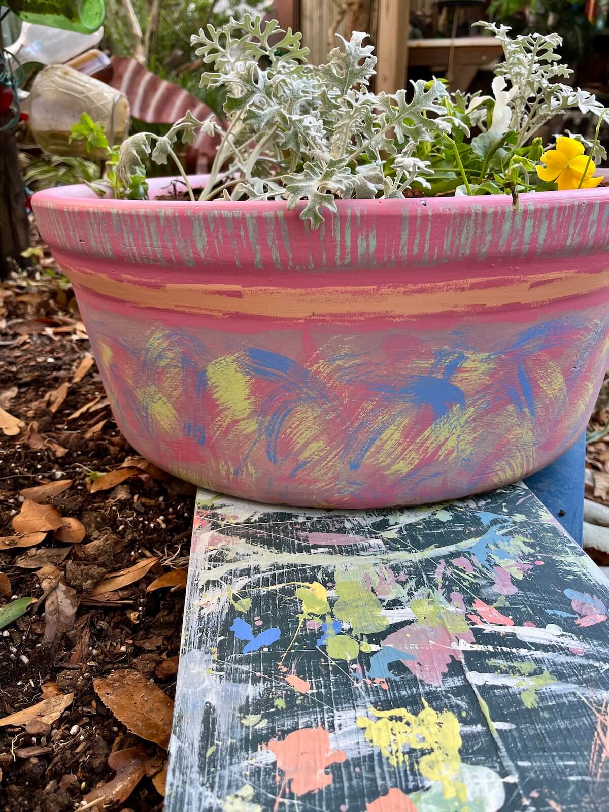 Hand painted clay pot on a paint-splattered board