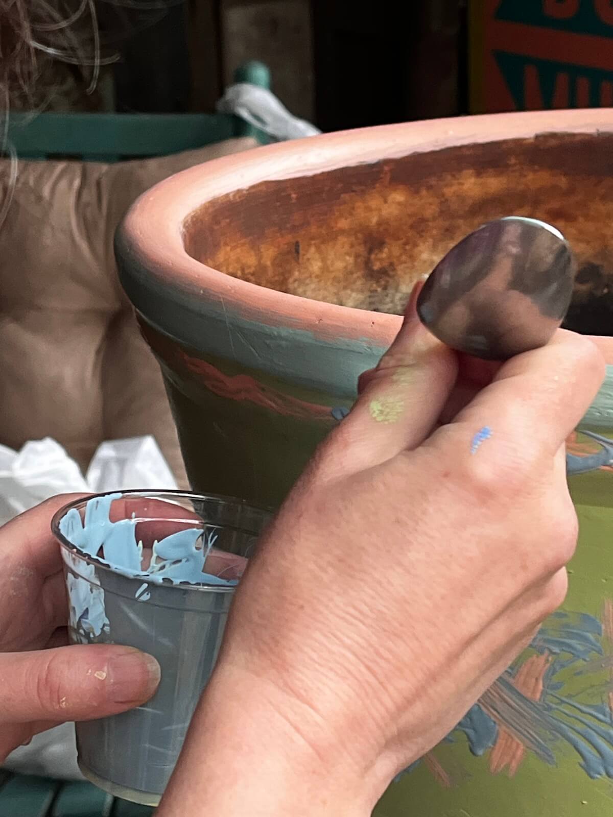 Using the handle end of a teaspoon to paint a band around a plant pot